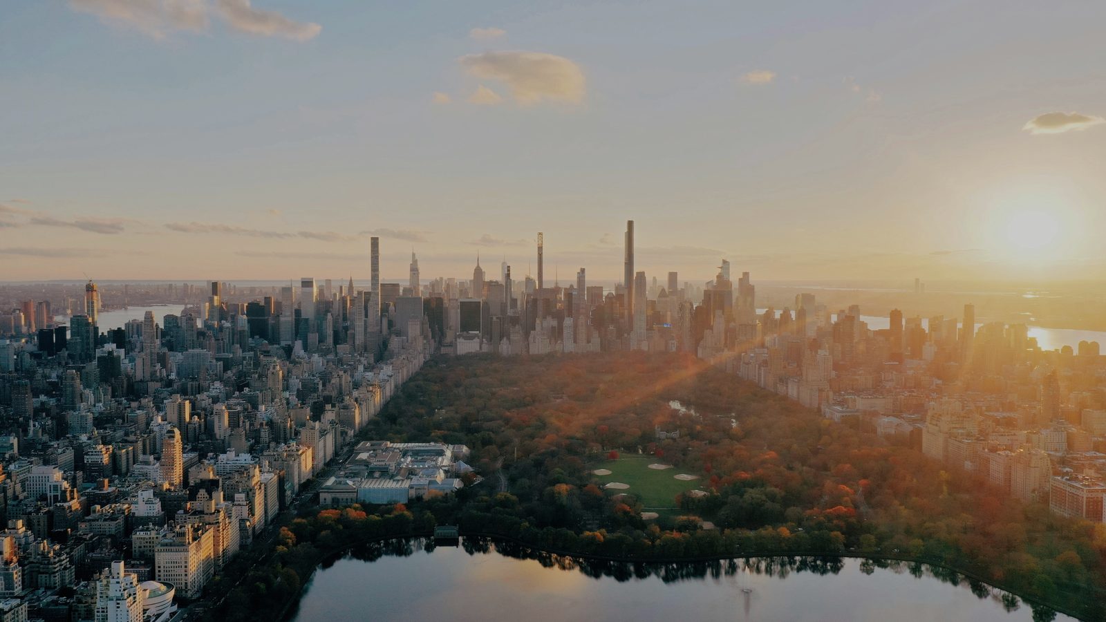 Central Park from the air at golden hour, with the Reservoir, autumn trees and the city skyline beyond.
