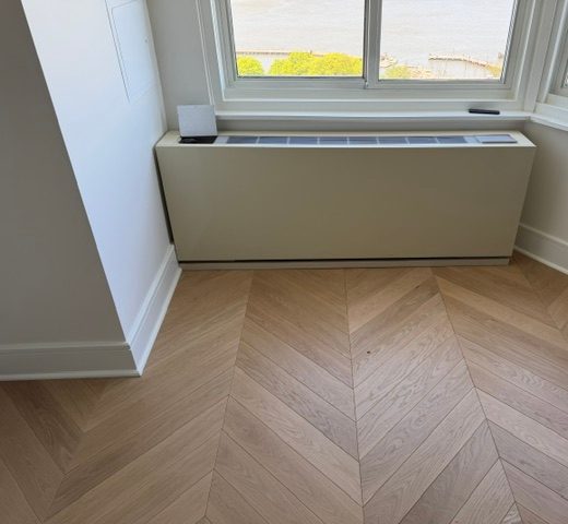 A cream-coloured cabinet under a bay window, above a herringbone wood floor.